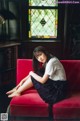 A woman sitting on a red couch in front of a window.