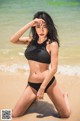 A woman in a black bikini sitting on the beach.