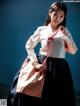 A woman in a white shirt and black skirt holding a pink bag.