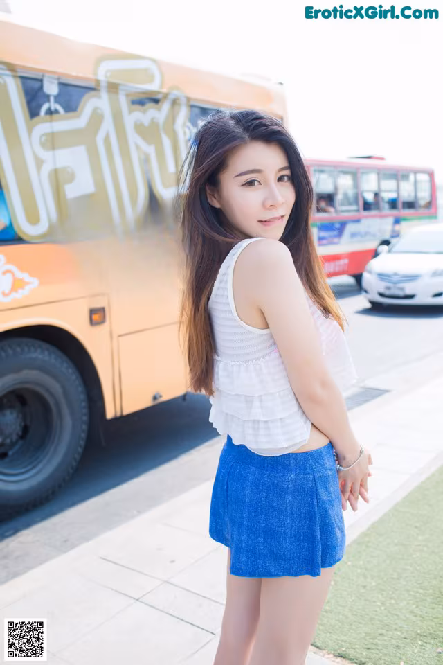 A woman standing in front of a bus on a city street.