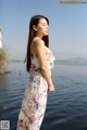 A woman in a floral dress standing by the water.