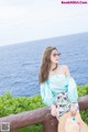 A woman sitting on a railing by the ocean wearing a straw hat.