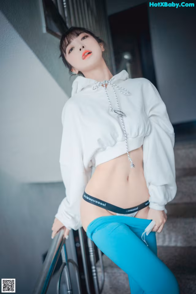 A woman in a white hoodie and blue pants posing for a picture.