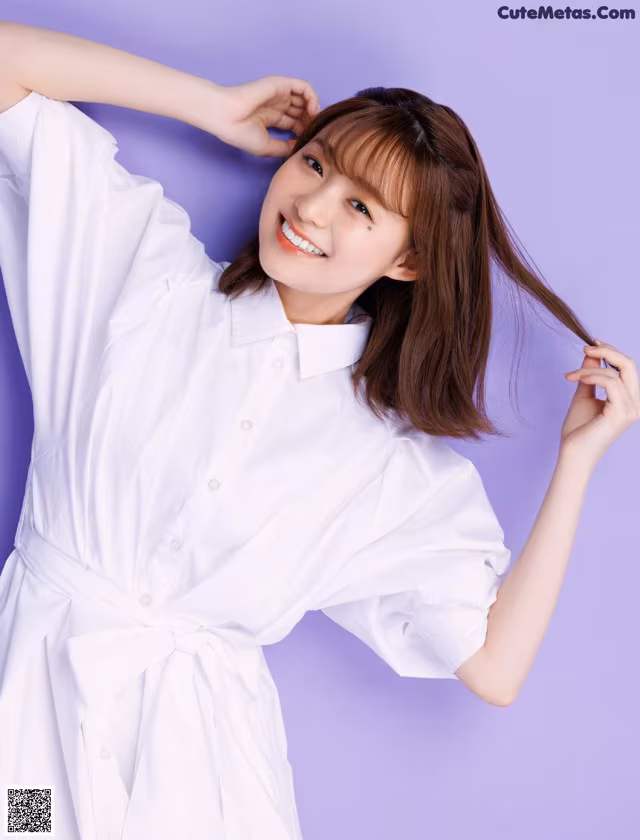 A woman in a white shirt dress posing for a picture.