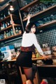 A woman standing in front of a bar holding a glass.